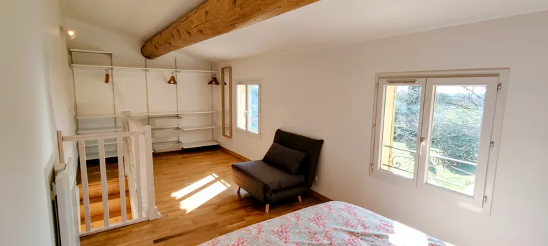 Chambre sous les poutres blanches, avec fauteuil près de la fenêtre