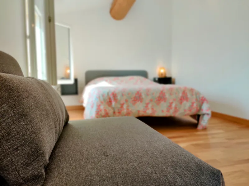 Fauteuil gris au premier plan et lit double en arrière-plan dans la chambre